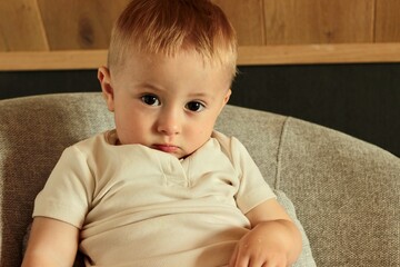 Portrait of a serious little boy sitting in a chair and looking at the camera