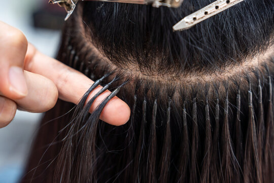 Professional female hairdresser shows keratin hair extensions tips to long-haired woman in hair salon. Professional hair extensions, keratin hair extensions on woman's fingers.