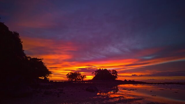 Time lapse A tranquil seascape during dawn at low tide under a serene sky transitioning from night to day. The sun slowly sets behind the island. The gradien sky changes color bright and colorful