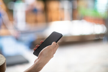 A black cell mobile phone in the hand of a young man in his twenties at a cafe with out of focus street scene in th background