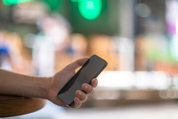 A black cell mobile phone in the hand of a young man in his twenties at a cafe with out of focus street scene in th background