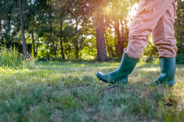 Woman in brown garden suit and green rubber boots walking thfough the autumn garden.