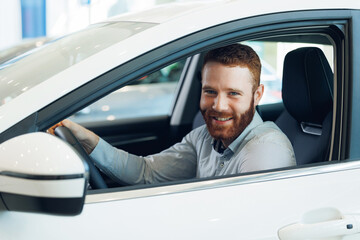 Business Handsome happy bearded man driver in showroom testing new car before buy