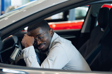 Handsome happy African American man is hug his new car and smiling in dealership