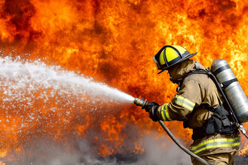 A firefighter in a protective fire suit with a fire extinguisher extinguishes a strong fire with water and protective foam from a hose.