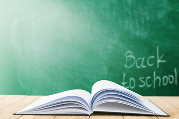Open black cover book or notebook against the background of a school green board with sunbeams. Back to school training concept. Empty background.