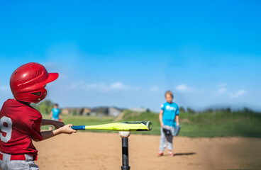 Youth batter hitting a tee ball into an open field at game