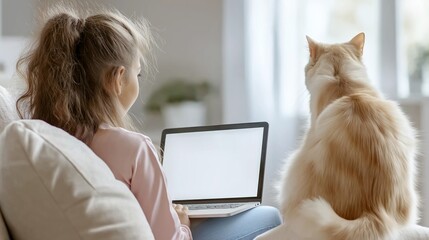 Fototapeta premium A girl is sitting on a couch with a laptop open in front of her. A cat is sitting next to her, looking at the screen. Concept of relaxation and companionship