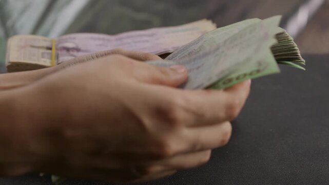 Hands sorting bundle of Bangladeshi Taka cash money, close up of business professional arranging stack of crisp BDT currency banknotes on wooden desk table
