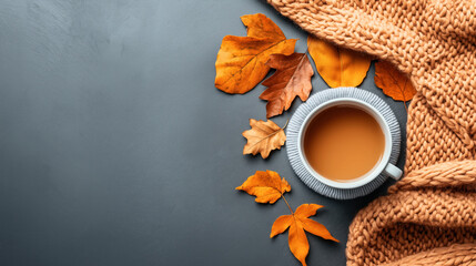 Top view of a cup of tea on a gray surface with autumn leaves and a knitted orange blanket. Cozy fall atmosphere with warm tones.