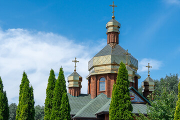Obraz premium Wooden church with golden domes and place religion of orthodox christian. Built structure for prayer in modern city. Landscape with green park and tower with cross. Ukrainian orthodox church in dnipro