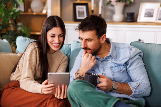 Couple reading online news using tablet computer and drinking morning coffee at home