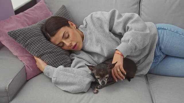 A young woman naps on a couch with her chihuahua in a cozy home interior.
