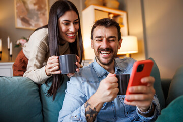 Couple doing online shopping using smart phone and drinking morning coffee at home