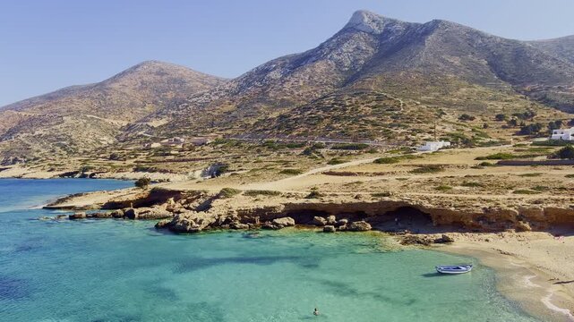 Warm sunlight dances on crystal-clear waters of Donousa, as gentle waves lap against the shore, inviting visitors to explore the tranquil beach.
