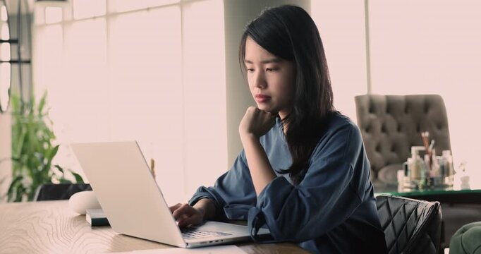 Young Asian woman sit at desk in modern workspace typing text on laptop keyboard, review and filling online schedule, focuses on completing tasks and projects, analyzing data, creating presentation