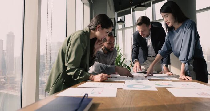Staff gather together in board room do data analysis review papers with charts and graphs, analyze financial infographic, create forecast, identify trends, share insights search solution, strategizing