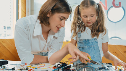Fototapeta premium Young smart caucasian teacher teaching students about part of electronic board. Expert girl learn about digital electrical tool and fixing motherboard at table with chips and wires placed. Erudition.