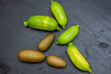 Ripe yellow and burgundy oblong citrus fruits on the black slate slab, close-up. Australian finger lime plant indoor growing. Microcitrus australasica, Faustrimedin