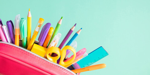 Fototapeta premium Back to school concept. Bright school pencil case with filling school stationery, pens, pencils, scissors, rule. School accessories on blue background. Flat lay, top view, copy space