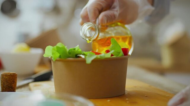 Chef preparing food dressing organic salad with olive oil. Healthy food preparation in vegetarian kitchen. Large palan paper container for food delivery. Disposable tableware recycling and disposal