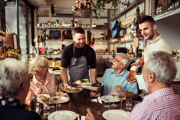 Happy senior friends being served food and wine at a restaurant