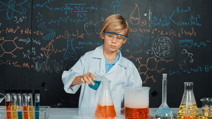 Smart boy inspect mixed chemical liquid in laboratory beakers while holding and looking carefully. Caucasian child focus on doing an experiment in chemistry lesson or STEM science class. Erudition.