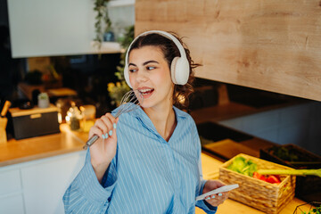 Young caucasian woman singing and listening to music in kitchen