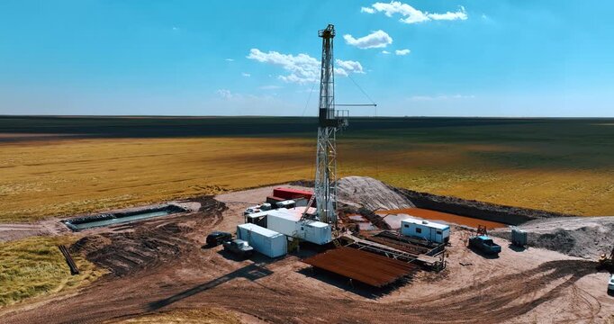 White metal derrick in the center of drilling site. Industrial production of oil or gas in the deserted area.