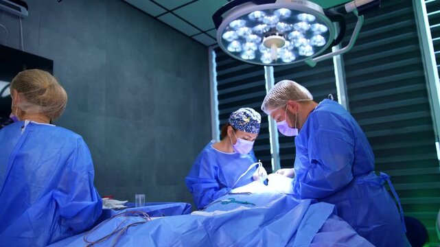 Assisting scrub nurse takes away used swabs at surgical operation. Medic helps at the procedure performed by two surgeons.