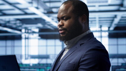 Admin in server farm using laptop to patch network issues leading to slow data transfer rates. Close up of IT specialist in data center workspace fixing errors affecting supercomputers, camera A