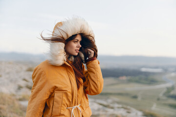 Fototapeta premium Woman in yellow coat talking on cell phone standing on hilltop with scenic view in travel mode