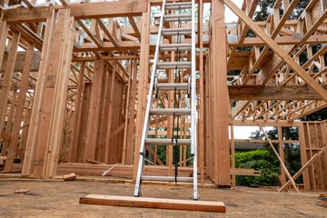 Interior new house construction at wood framing stage, aluminum extension ladder propped up on 2nd floor support truss beams

