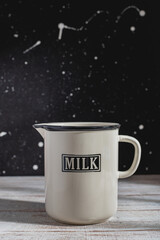 Enamel milk cream jug. Wooden table. White dots and splashes on black background.