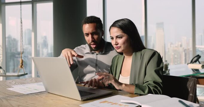 Two multiethnic colleagues collaborate on project using laptop, involved in brainstorm, researching information, analyzing data, making decisions, share insights, discuss strategies and allocate tasks