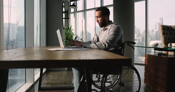 Man in wheelchair efficiently manages his tasks using laptop, search issue solution, learn new program, review documents, communicating through emails, analyze data, completing reports. Telecommuting