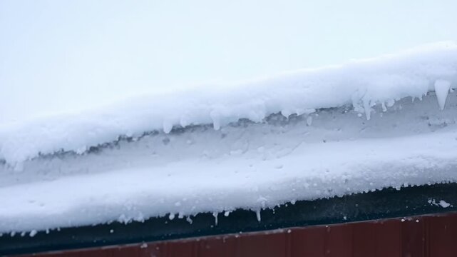 A snowy rooftop where the snow is piling up in distinct layers with some melting and dripping down the sides.