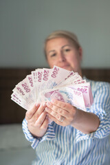 woman holds large stack of 200 Turkish lira bills in front of her, spreads it with a fan and shows...