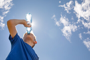child boy drinking water from bottle outdoors on a hot sunny day 