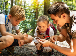 Family father two kids boy and girl siblings looking discovering exploring nature through magnifying glass, parent child during outdoor hike in the forest learning about nature 