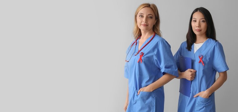 Female doctors with red ribbons on grey background. AIDS awareness concept
