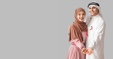 Muslim couple with red ribbons on grey background. AIDS awareness concept