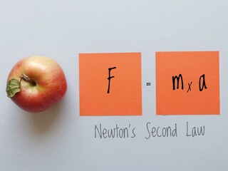 Newton's second law of motion formula on orange sticky notes with apple. Force, mass and acceleration equation. Force is equal to mass times acceleration. Physics formula, education concept.