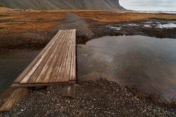 Old wooden footbridge is crossing a small stream leading towards the ocean in a volcanic landscape © Eclipsnet