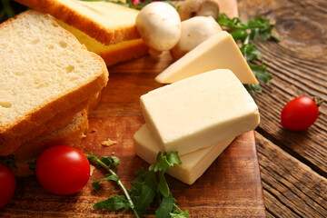 Board with processed cheese, bread and vegetables on brown wooden background