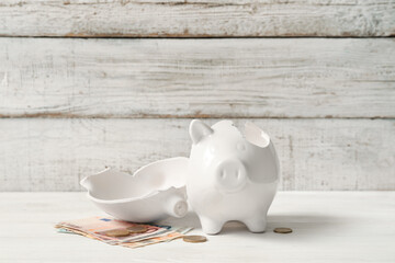 Broken piggy bank with money on white wooden background. Concept of bankruptcy