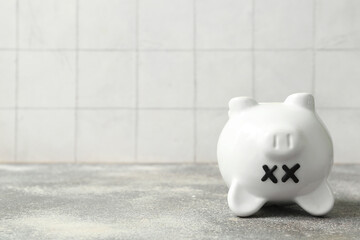 Piggy bank with closed eyes  on grunge table near white tile background. Concept of bankruptcy