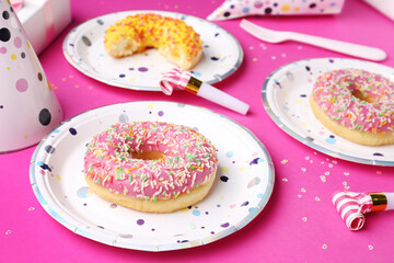 Paper disposable plates with donuts and party blowers on pink background, closeup