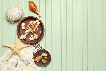 Plates with sea shells, starfish and newspaper on green wooden background