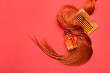 Obraz premium Ginger hair strand, comb and bottle of essential oil on red background